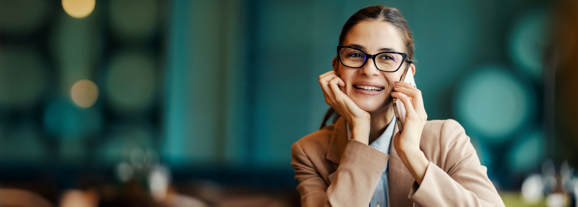 Portret van een gelukkige jonge vrouw die in een café zit en een aangenaam telefoongesprek voert.